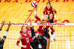 Female volleyball player is at the net spiking the ball.